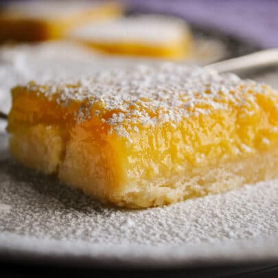 A lemon bar that's been dusted with powdered sugar resting on a white plate.