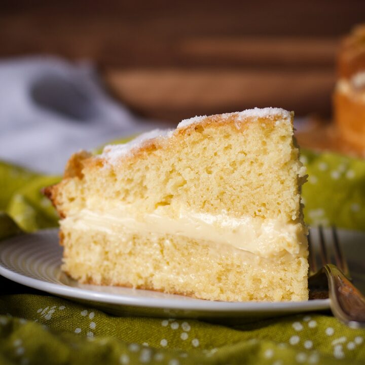 A slice of olive oil cake filled with lemon mascarpone pastry cream on a plate, ready to eat.