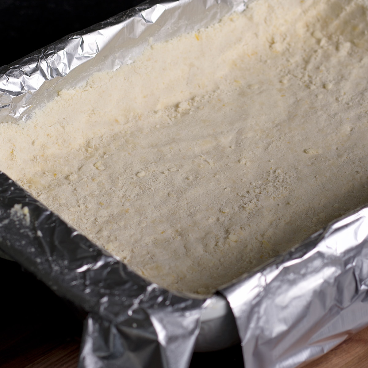 Pressing the raw shortbread dough into the bottom of a prepared baking dish.