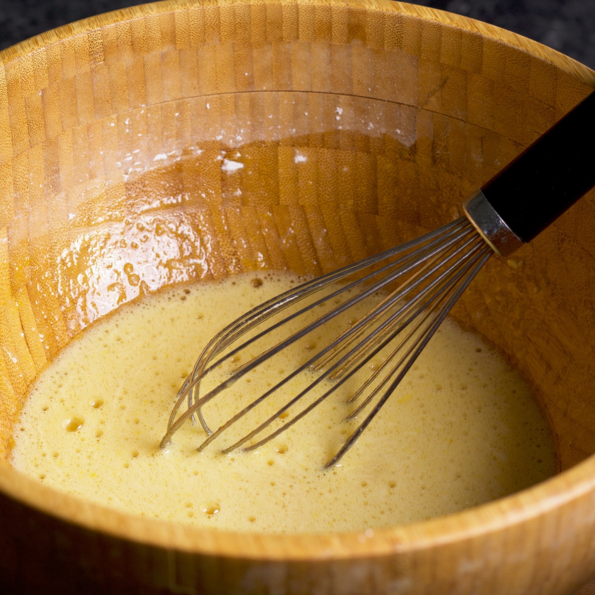 Whisking eggs, sugar, and flour in a wood bowl to make the batter for lemon bars.
