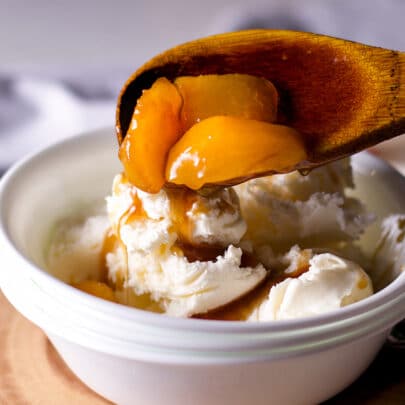 Spooning roasted fruit in brown butter maple sauce over vanilla ice cream.