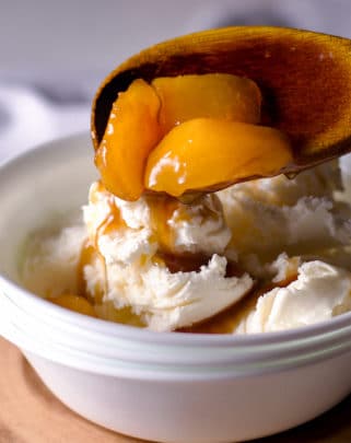 Spooning roasted fruit in brown butter maple sauce over vanilla ice cream.