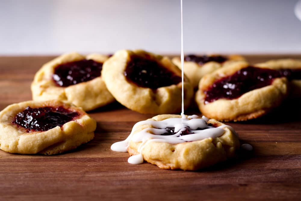 Drizzling almond glaze over thumbprint cookies filled with cherry jam.