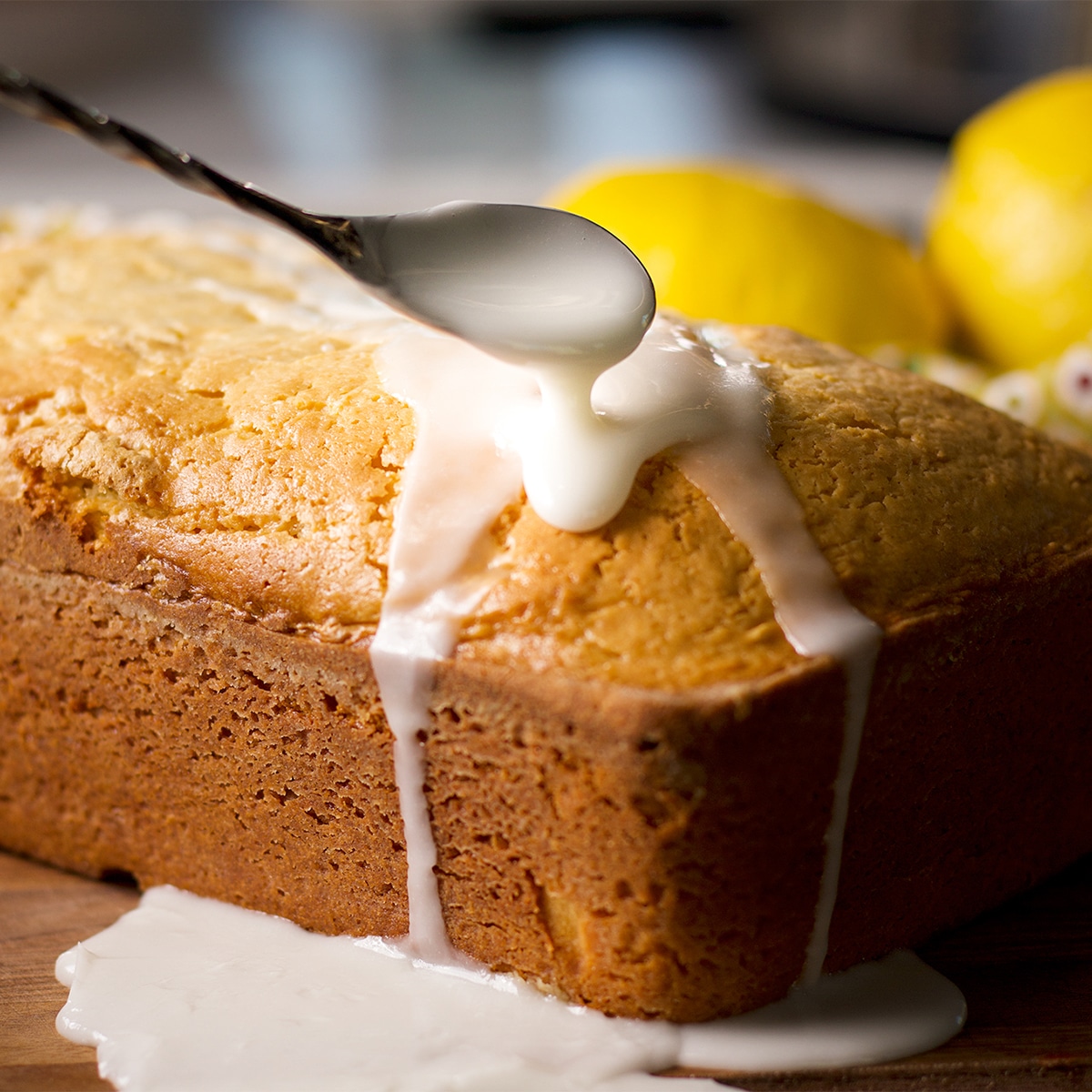 Using a spoon to drizzle lemon glaze over the top of a lemon loaf cake.