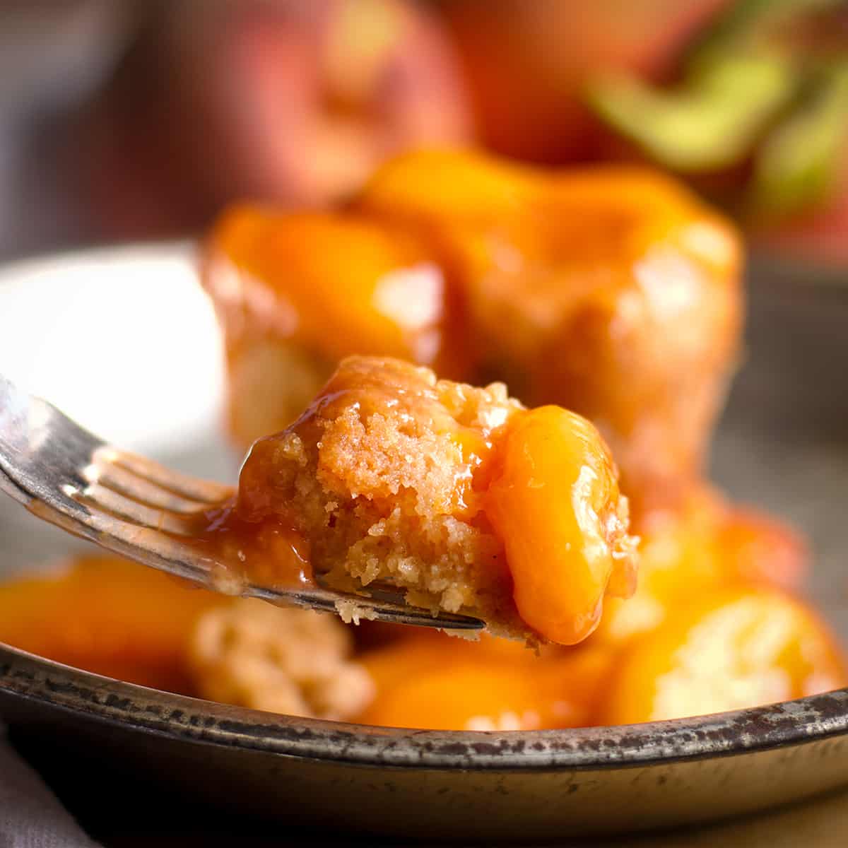 Someone using a fork to take a bite of a peach cobbler muffin smothered in peach sauce.