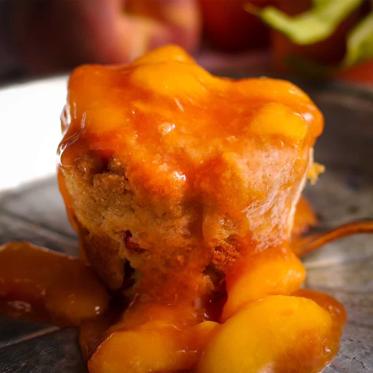 A peach cobbler muffin smothered in peach sauce on a tin plate.