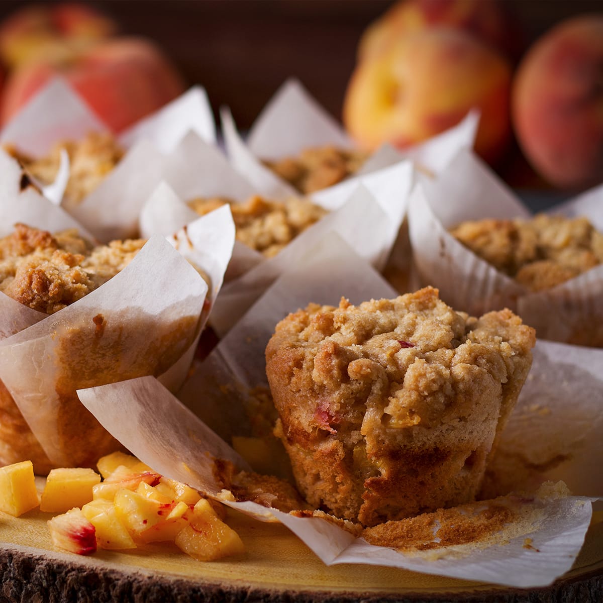A wood tray filled with freshly baked peach cobbler muffins. One of the muffins is unwrapped so you can see the cobbler topping.