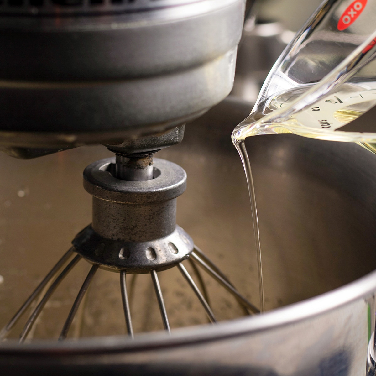 Pouring olive oil into cake batter while an electric mixer beats the oil into the batter.