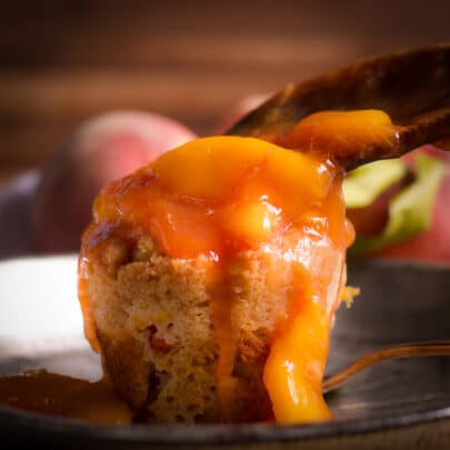Someone spooning peach sauce over the top of a peach cobbler muffin.