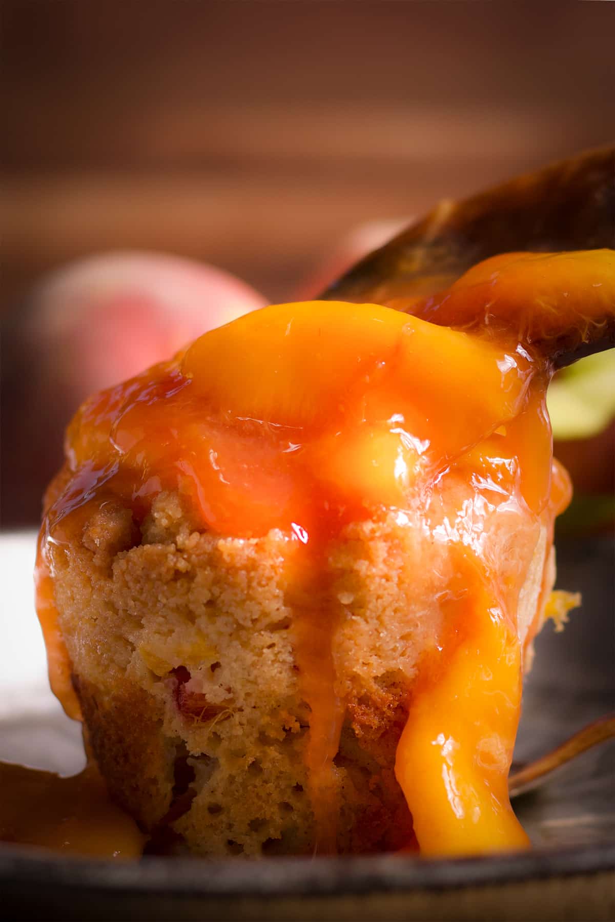 Someone spooning peach sauce over the top of a peach cobbler muffin.