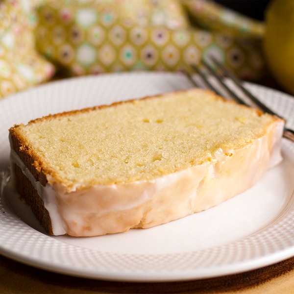 A slice of lemon loaf cake on a plate with a fork, ready to eat.