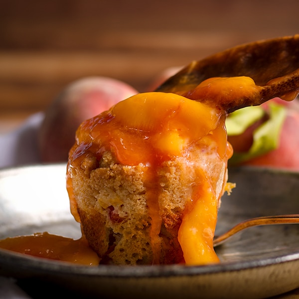Spooning peach sauce over the top of a peach cobbler muffin.