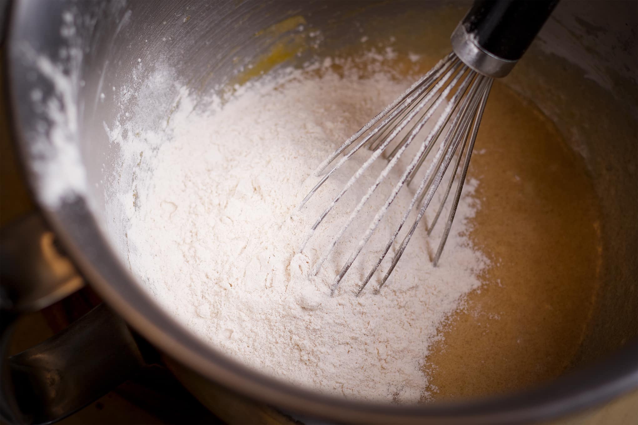 Someone using a wire whisk to mix flour into peach muffin batter.