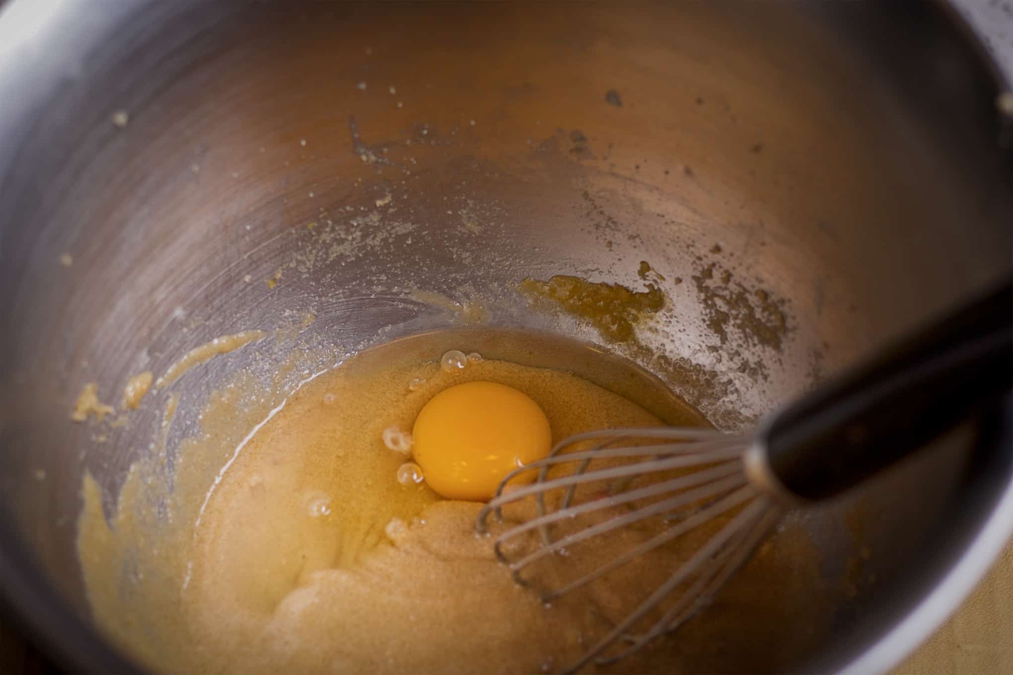 Someone using a wire whisk to beat an egg into peach muffin batter.