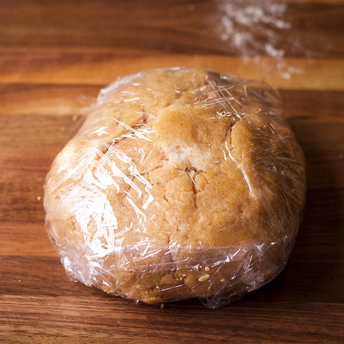 A ball of toasted almond pie crust pastry wrapped in plastic wrap.