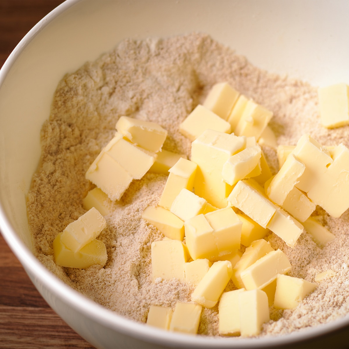 Pieces of cold butter piled on top of flour inside a white mixing bowl.
