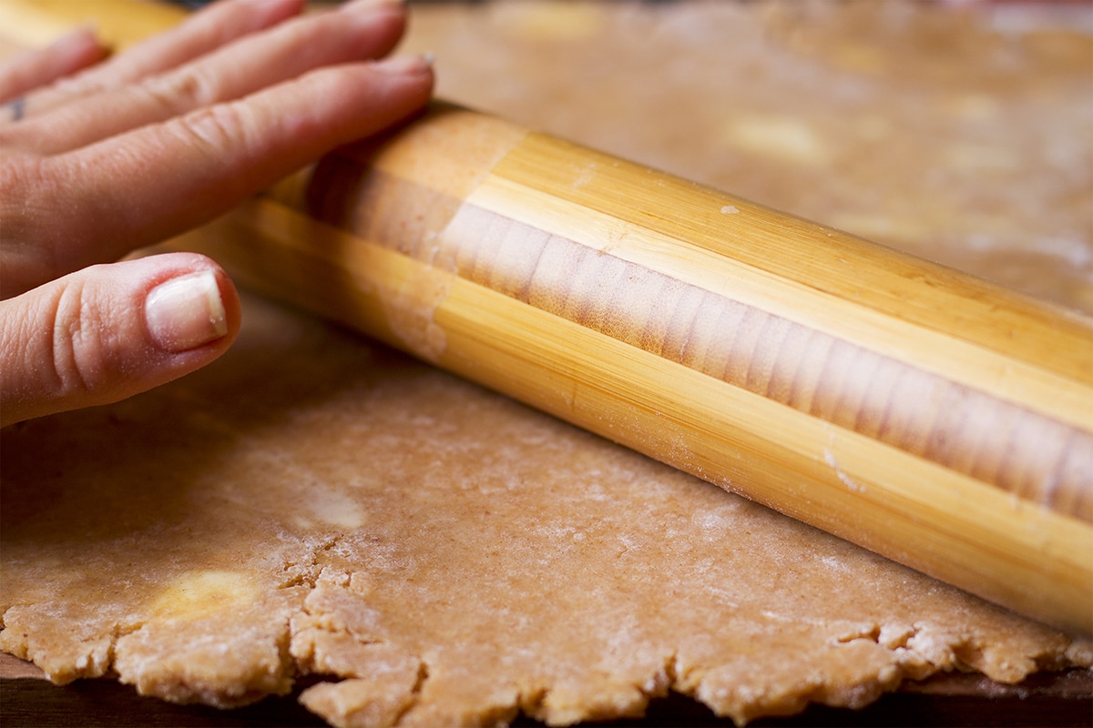 Someone using a wooden rolling pin to roll out toasted almond pie crust dough.