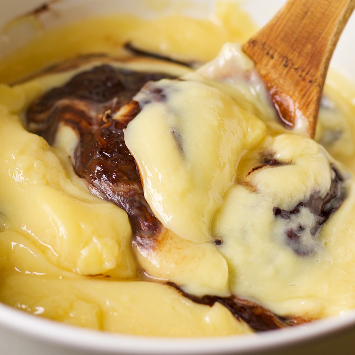 Using a wooden spoon to stir hot pastry cream into melted chocolate.