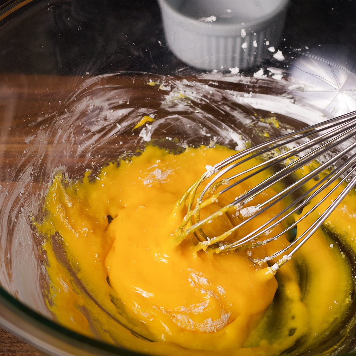 Using a wire whisk to mix corn starch and egg yolks in a glass bowl.