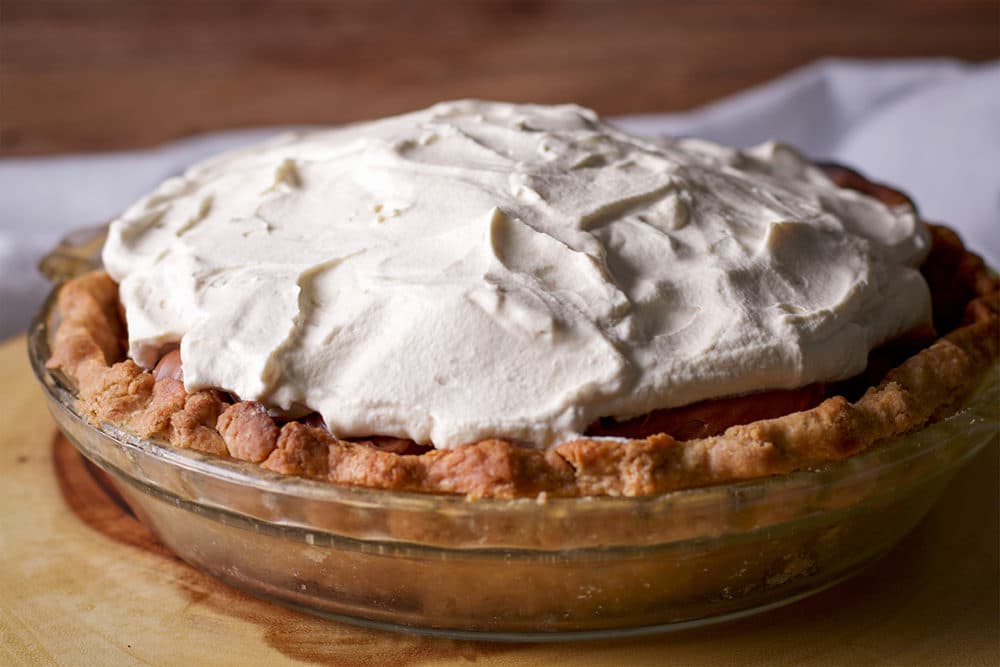 A Chocolate Cream Pie with whipped cream topping sitting on a wood board, ready to serve.
