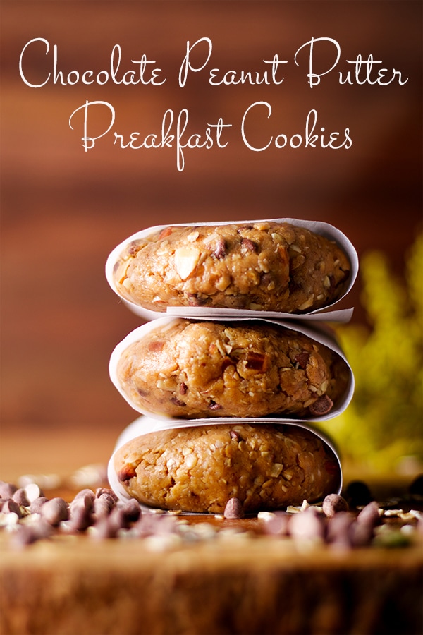 Three parchment wrapped no-bake, high protein breakfast cookies stacked on top of each other on a wooden tray.