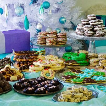 A table filled with platters piled high with different kinds of Christmas cookies.