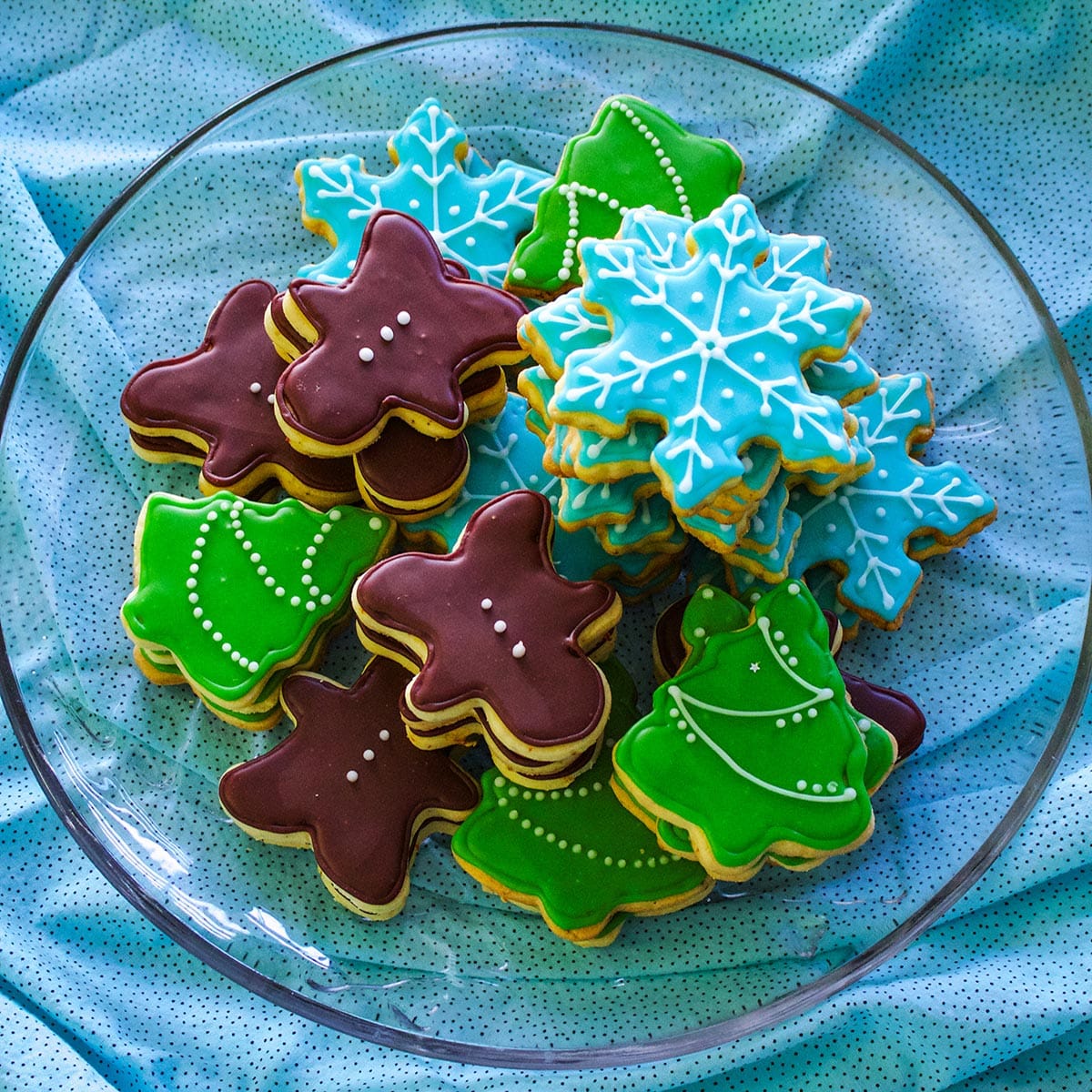 A glass plate filled with brown butter frosted ad decorated Christmas cookies.