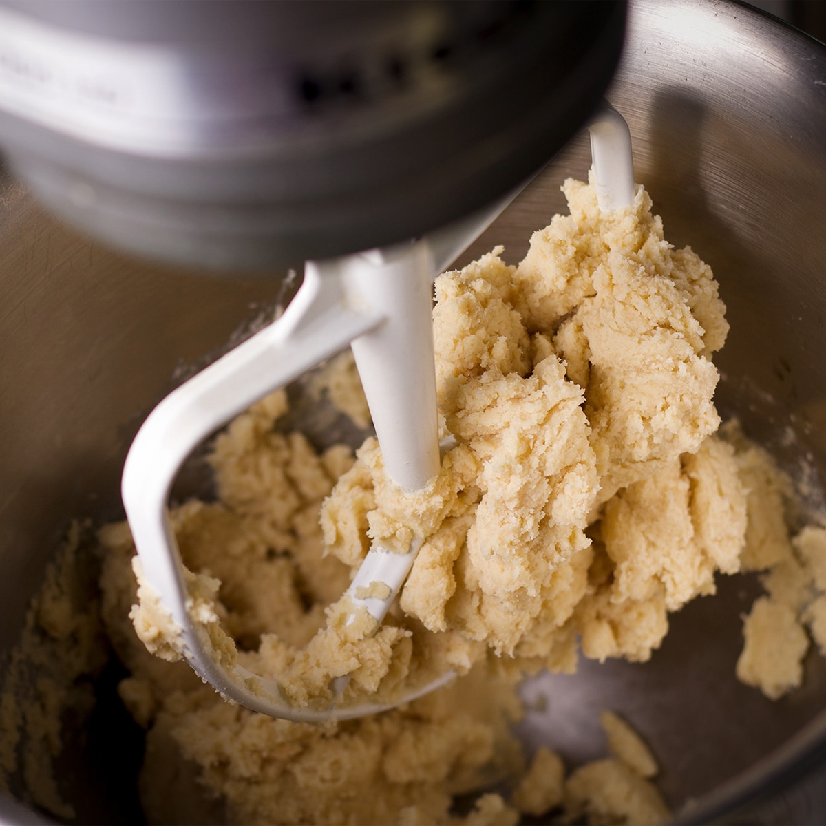 Looking down into the bowl of an electric mixer as it beats shortbread dough.