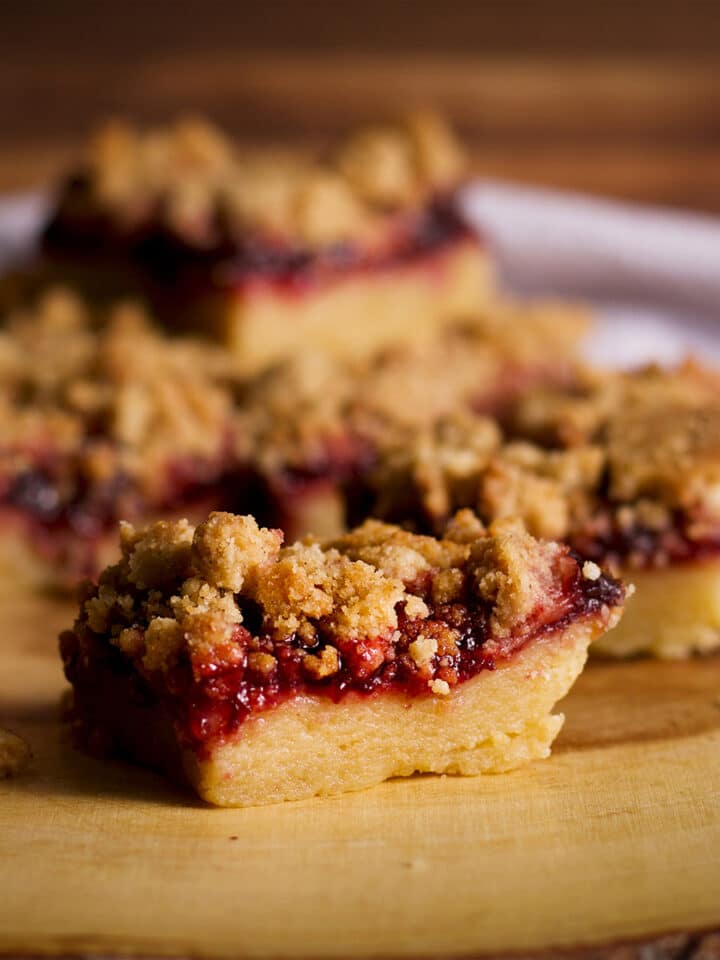 A wood serving platter stacked with cherry shortbread crumble bars.