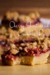 A cherry shortbread crumble bar on a tray with a bite taken out of it.