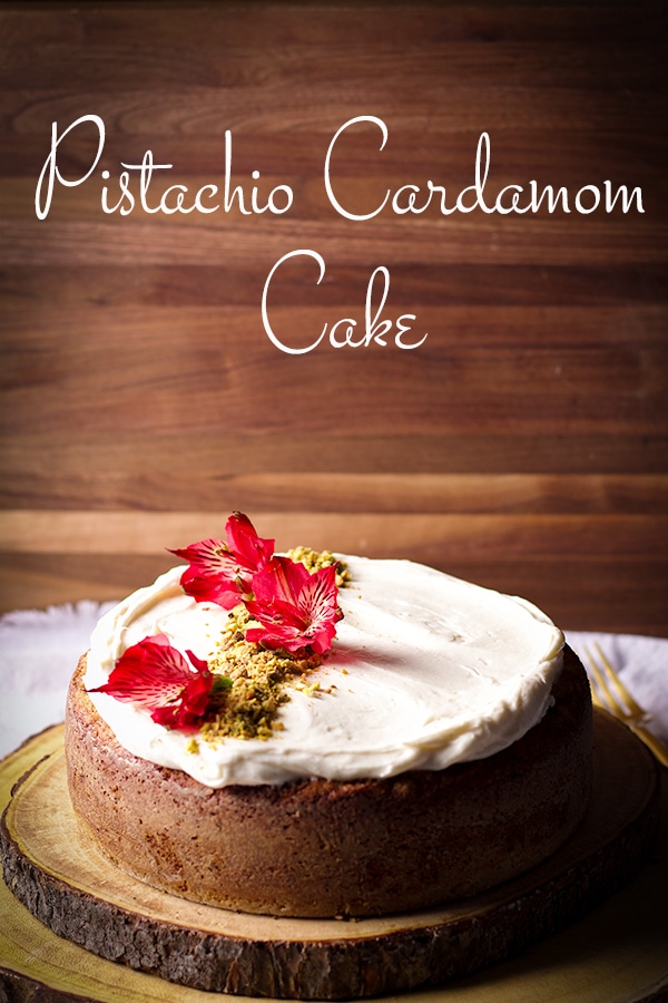 A Pistachio Cardamom Cake frosted with Cream Cheese Buttercream on a wooden tray. 