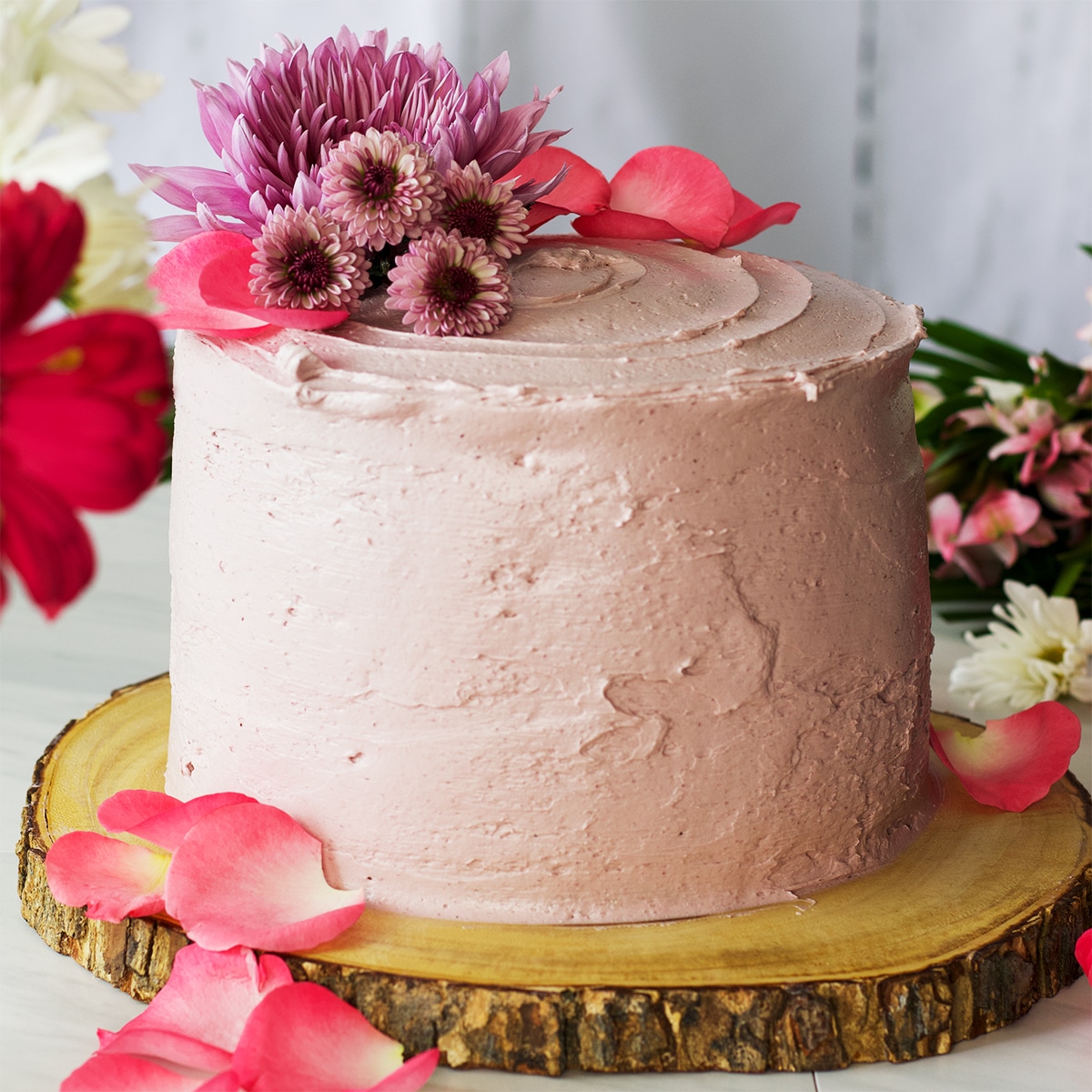 A lemon layer cake frosted with blackberry buttercream and decorated with fresh flowers.