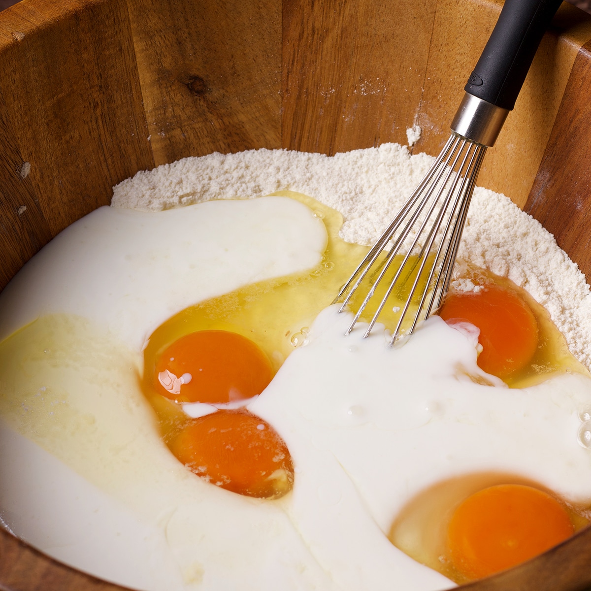 Adding eggs and buttermilk to flour to make pancakes.
