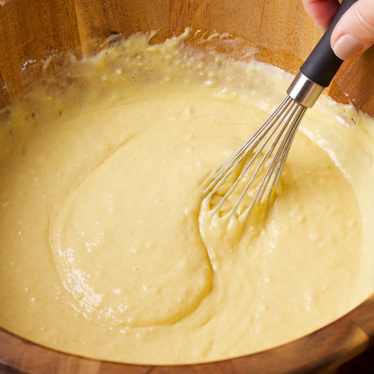 Using a wire whisk to mix pancake batter in a wood bowl.
