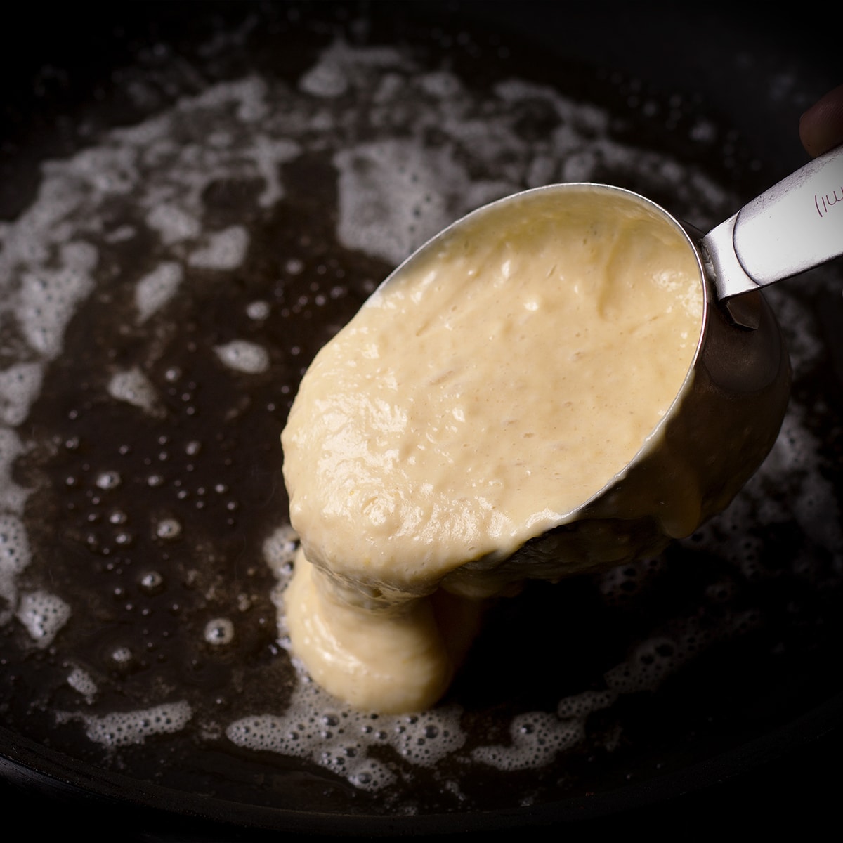Using a measuring cup to pour pancake batter into a hot skillet.