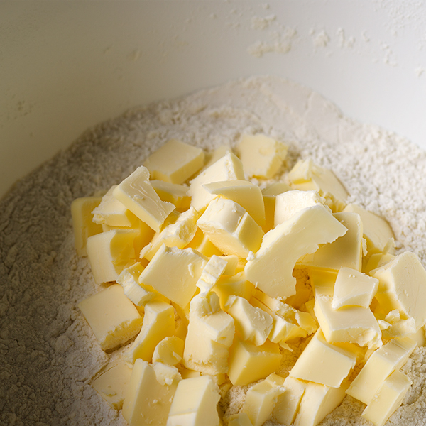 Adding cold butter to the dry ingredients to make buttermilk biscuits.