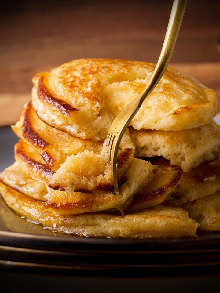 A plate of pancakes covered in syrup with a fork cutting into the stack of pancakes.