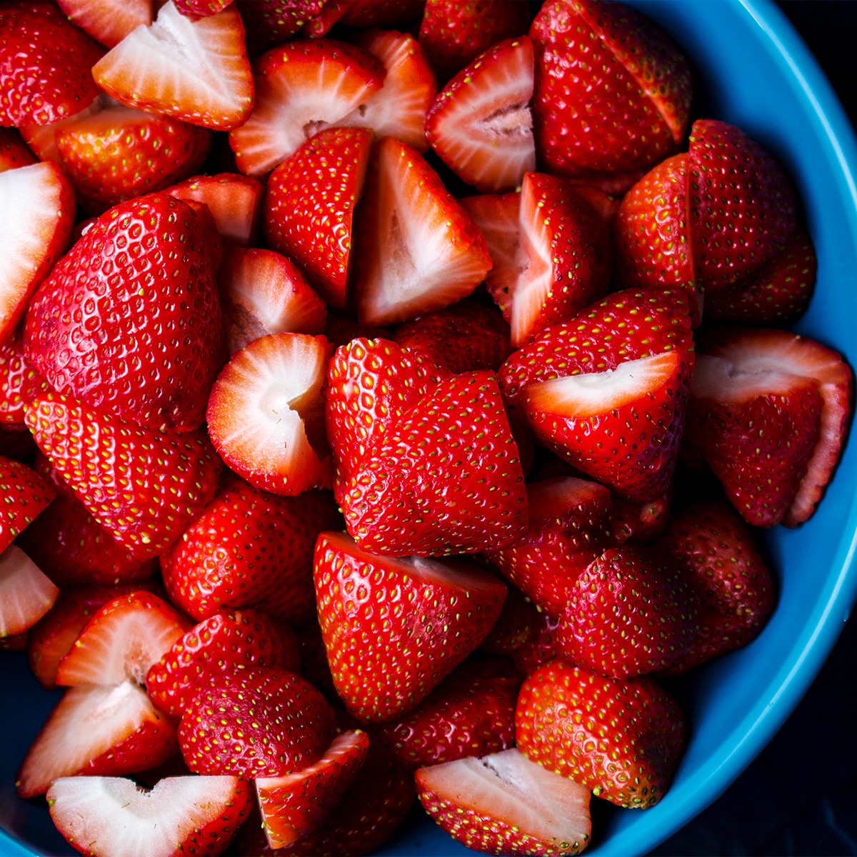 A bowl of bright red, ripe strawberries that have been cut in half.