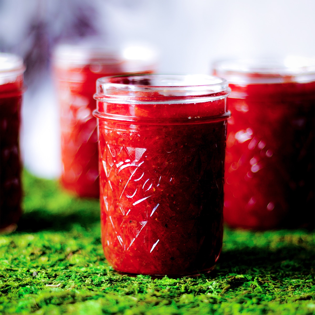 Jars of strawberry rhubarb jam sitting on a table covered with bright green artificial grass.
