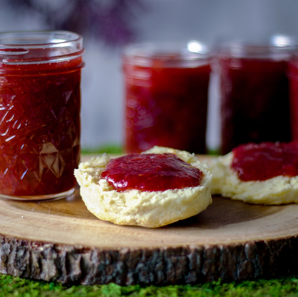 Homemade strawberry rhubarb jam spread over two halves of a buttermilk biscuit that's been cut in half.