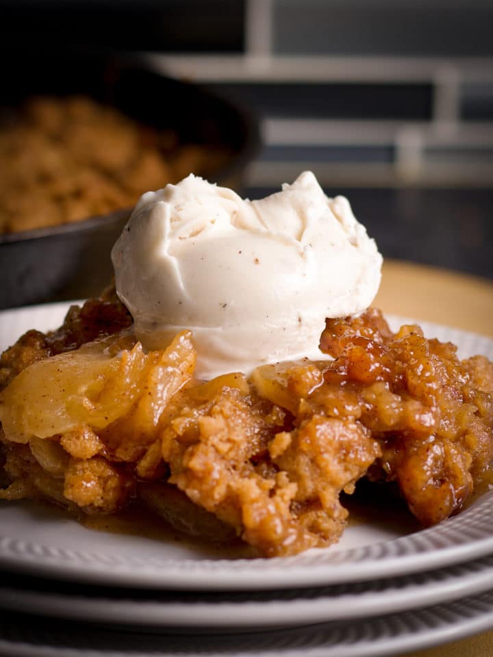 A serving of homemade apple cobbler on a plate, topped with a scoop of vanilla ice cream.