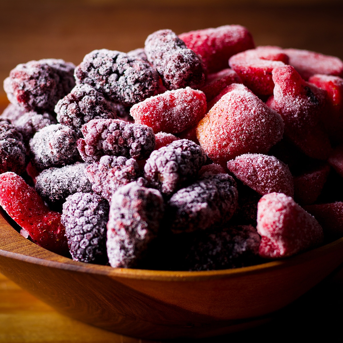 A wood bowl filled with frozen mixed berries.