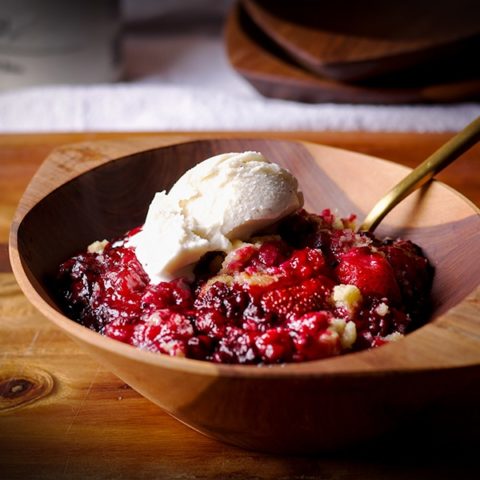 A wood bowl filled with berry cobbler and a scoop of vanilla ice cream.