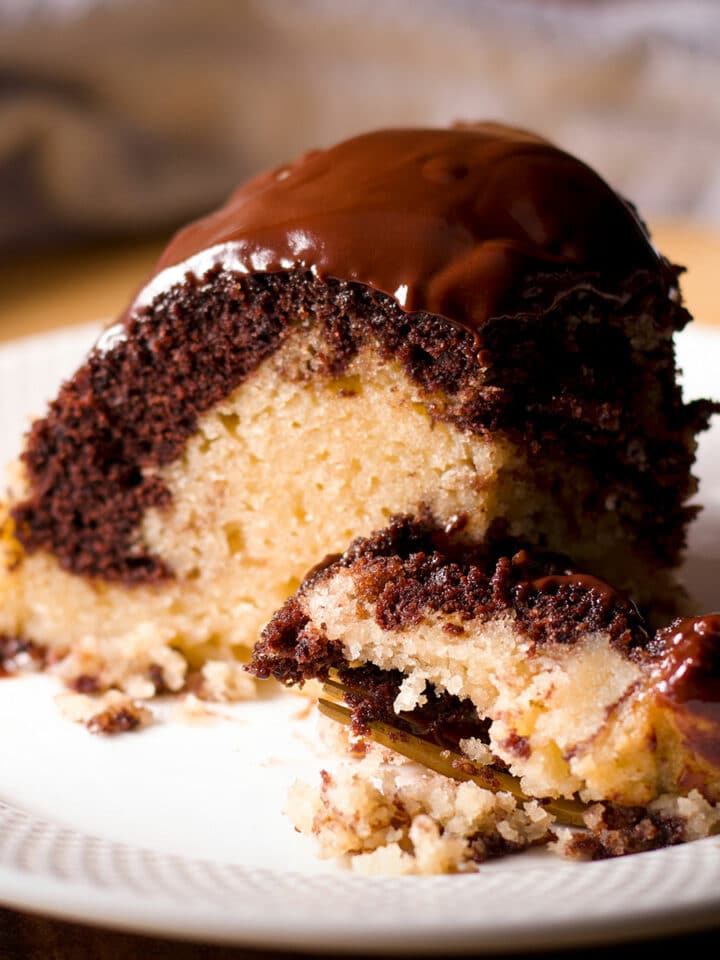 Someone using a fork to cut a bite from a slice of chocolate marble cake.