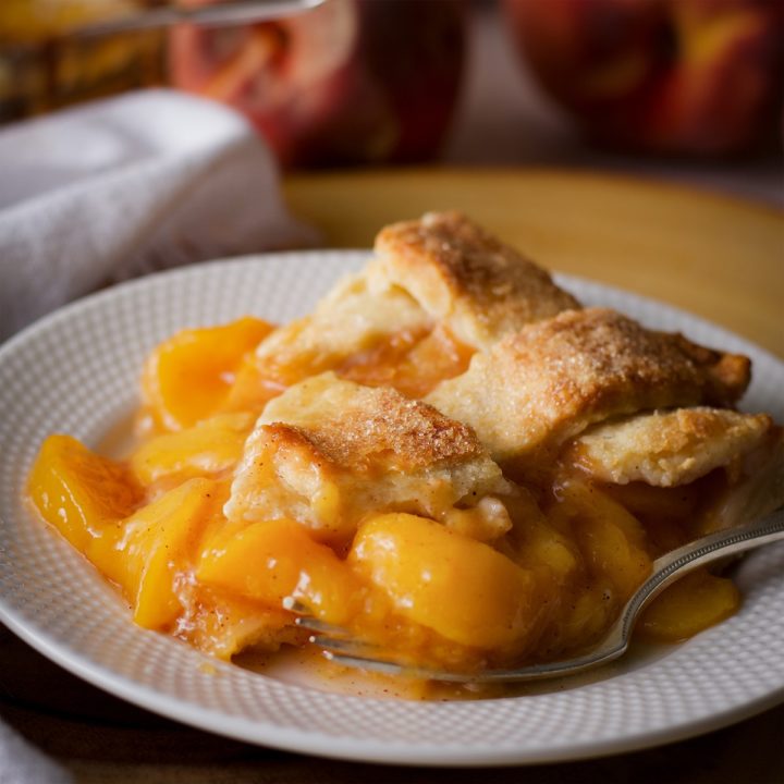 A slice of peach pie with a lattice crust on a plate.