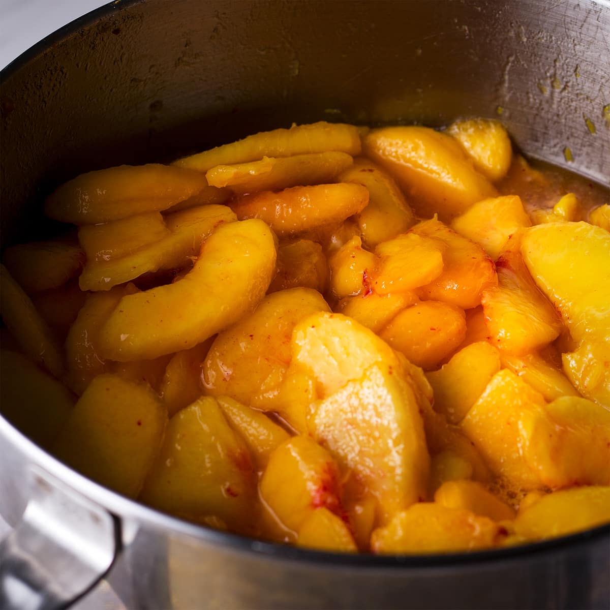A large saucepan filled with sliced, fresh peaches.
