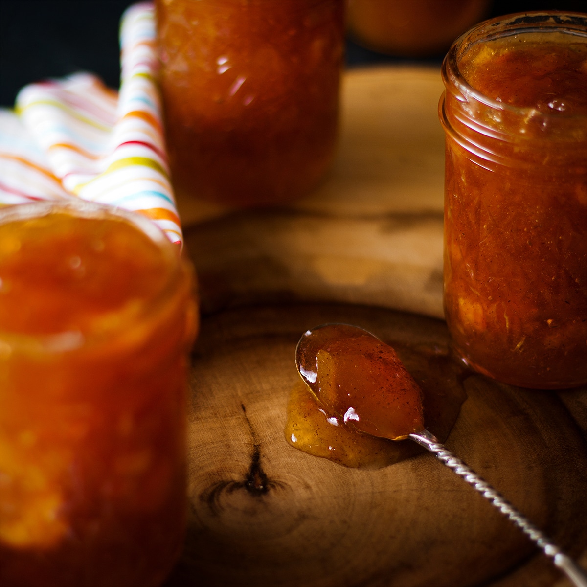 A spoonful of homemade peach preserves resting on a wood table next to several jars of peach preserves.