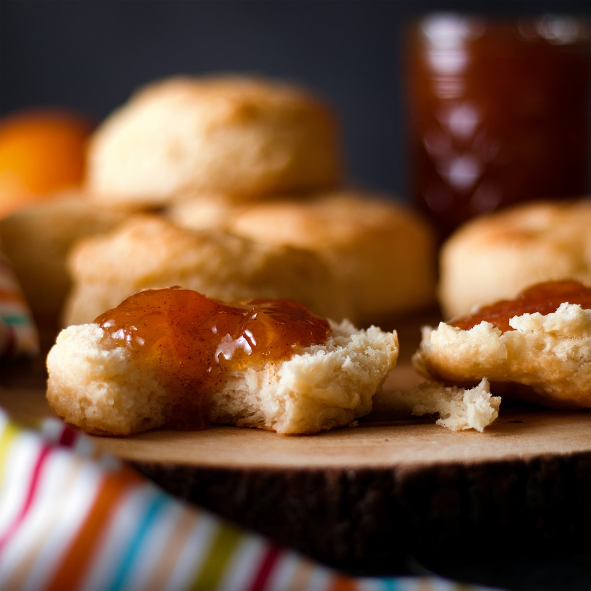 A buttermilk biscuit spread with homemade peach preserves with a bite taken out of it.