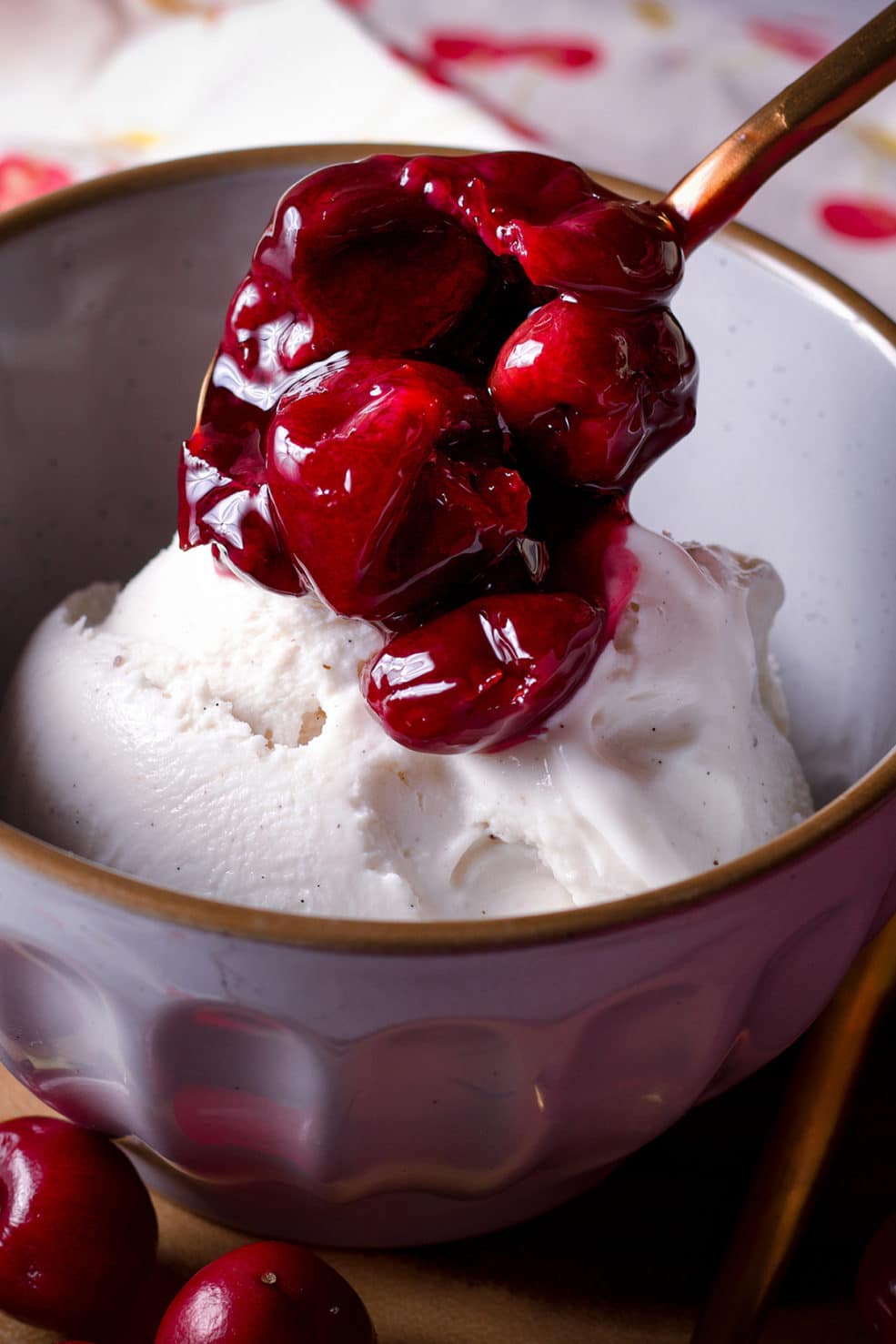 Spooning cherry sauce over a bowl of vanilla ice cream.