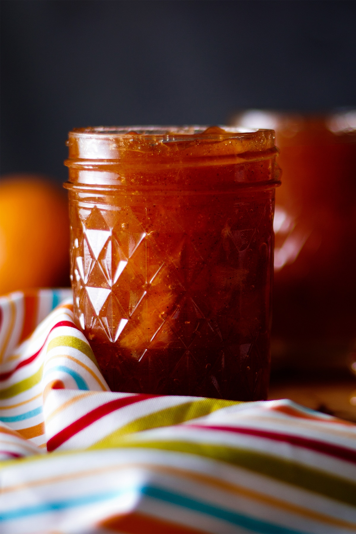 A jar of homemade peach preserves resting on a table covered with a colorful striped tablecloth.